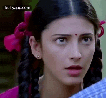 a close up of a woman 's face with braids and a pink flower in her hair .