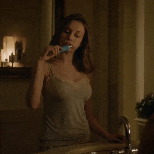 a woman in a tank top is brushing her teeth