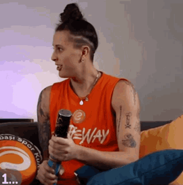 a woman is sitting on a couch holding a baseball bat and wearing an orange jersey that says ' beway ' on it
