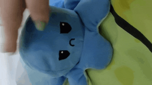 a person is holding a blue stuffed animal with a black face on a green surface .
