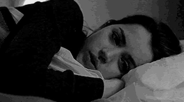 a black and white photo of a woman laying on a bed .