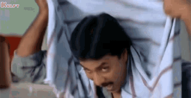 a man is holding a towel over his head and making a face .