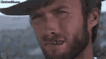 a man with a beard is smoking a cigarette and wearing a hat .