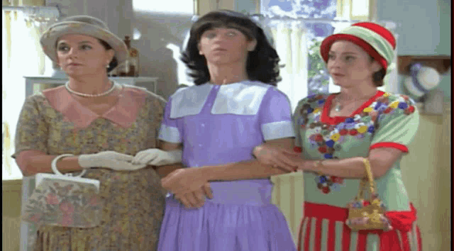 a man in a purple dress stands between two women in hats