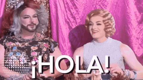 a man and a woman are sitting next to each other in front of a pink curtain and a sign that says hola !