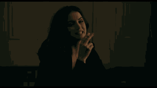 a woman in a black jacket is smoking a cigarette in a dark room