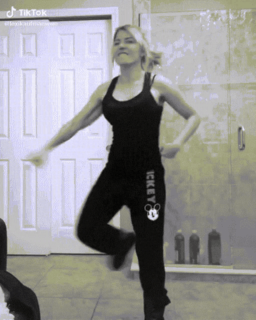 a woman in a black tank top and black mickey mouse sweatpants is dancing in front of a door