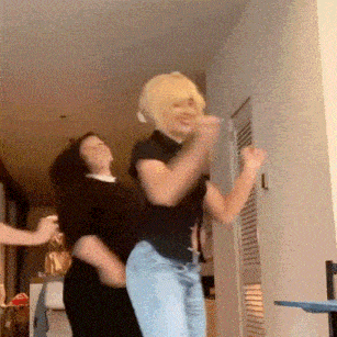 two women are dancing together in a room and one of them is wearing a blonde wig .