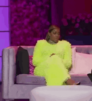 a woman in a neon yellow fur coat is sitting on a couch holding a cell phone .