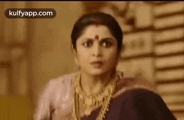 a close up of a woman wearing a purple saree and gold jewelry .