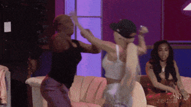 two women are dancing in front of a purple wall that says zeus on it