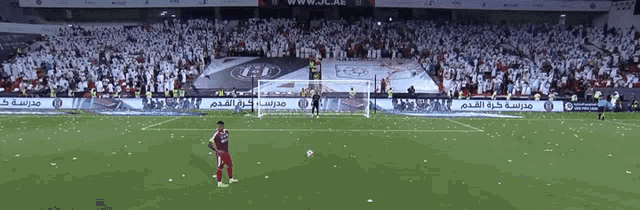 a soccer player stands on the field in front of a crowd with a banner that says www.jc.ae on it