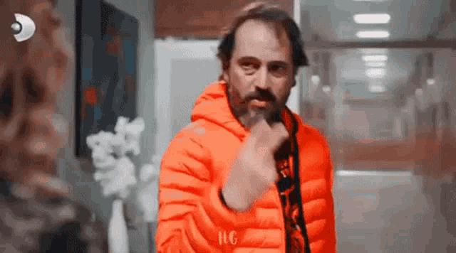 a man in an orange jacket is giving the middle finger to a woman .