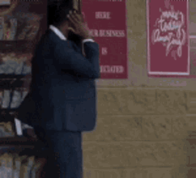 a man in a suit is talking on a cell phone in front of a sign that says make today amazing .