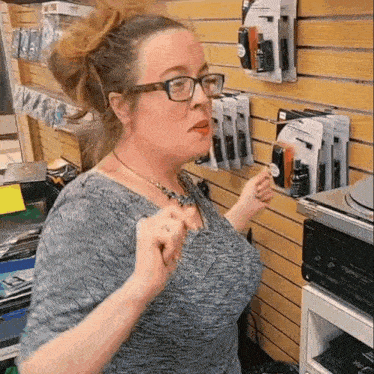 a woman wearing glasses and a necklace is standing in front of a wall with a bunch of products on it .