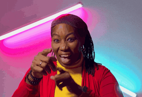 a woman wearing a red jacket and a yellow sweater is pointing at the camera