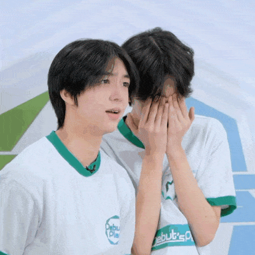 a boy covering his face with his hands while wearing a shirt that says debut 's