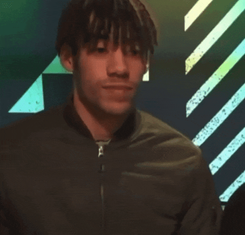 a young man wearing a black jacket stands in front of a green and white striped background