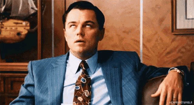 a man in a suit and tie is sitting in a chair with his hands on his hips
