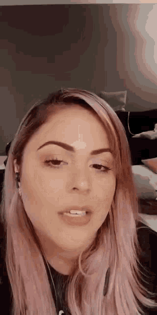 a woman with pink hair is wearing headphones and a black shirt and looking at the camera .