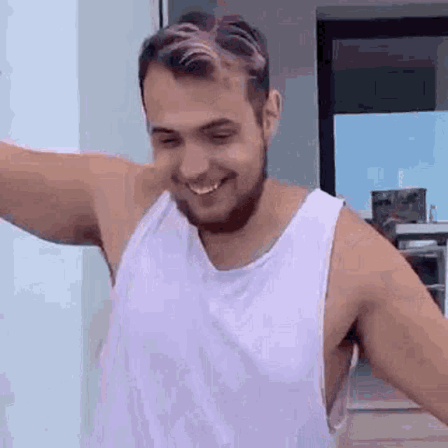 a man with a beard and pink hair is wearing a white tank top and smiling .
