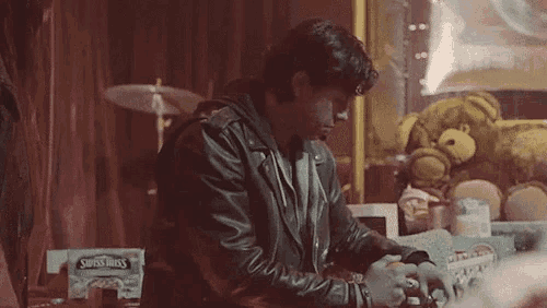 a man in a leather jacket is sitting at a table in front of a candy machine .