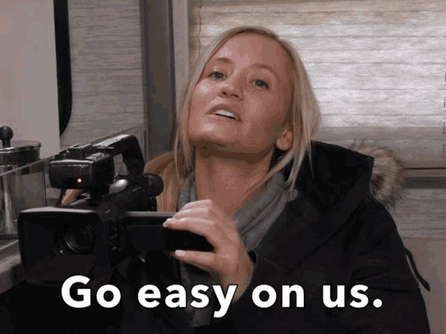 a woman holding a camera with the words go easy on us written below her