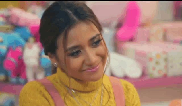 a woman wearing a yellow sweater and pink overalls is smiling in front of a display of stuffed animals .