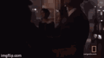 two men in suits and ties are standing next to each other in a dark room .