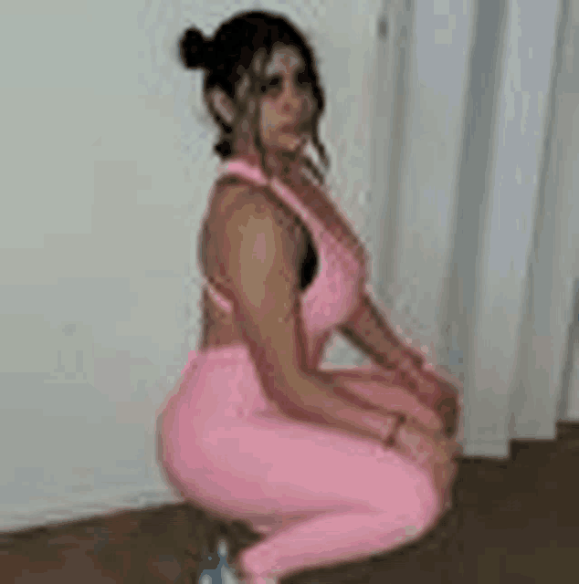 a woman in a pink outfit is squatting on the floor .