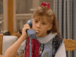 a young girl is talking on a blue telephone while sitting at a table .