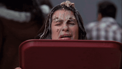 a woman with icing on her face is holding a red container