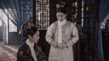 two women are standing next to each other in a room and talking to each other .