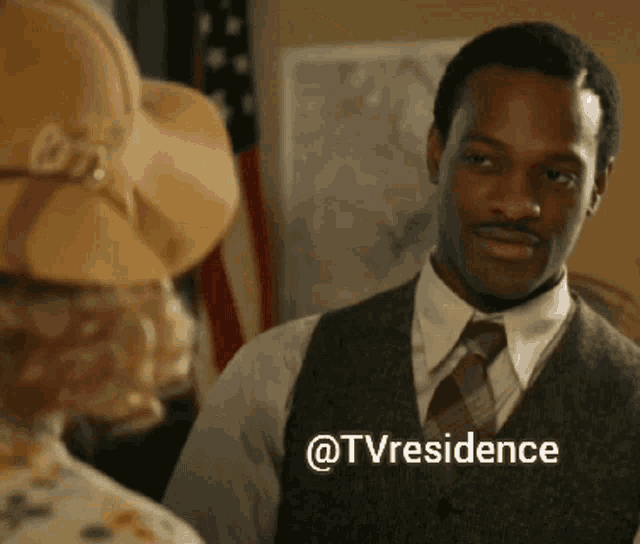 a man in a suit and tie is standing next to a woman in a hat and says " @tvresidence "