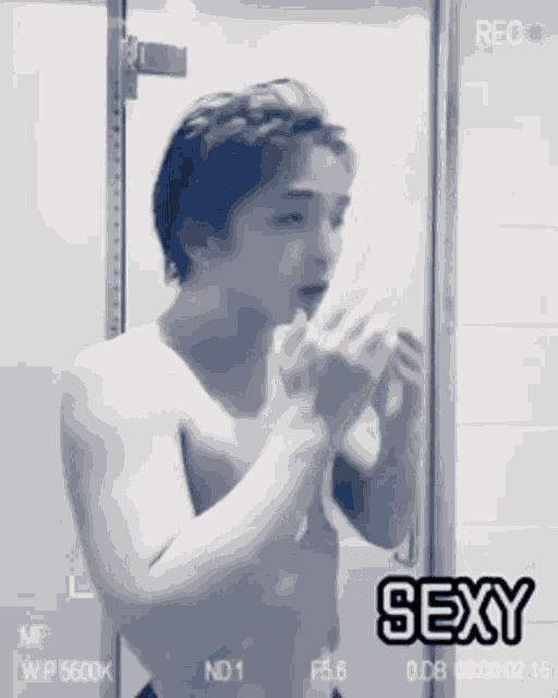 a shirtless man is looking at himself in a mirror with the words sexy on the bottom right