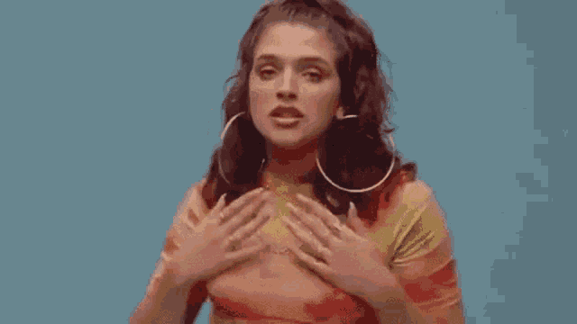 a woman in a tie dye shirt and hoop earrings is holding her chest .