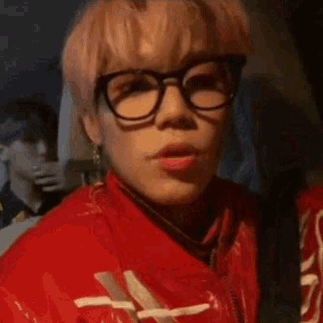 a young man with pink hair and glasses is wearing a red jacket .