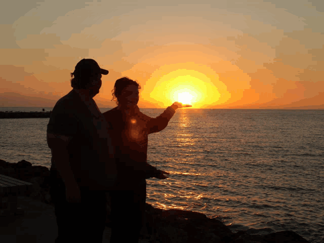 a man and a woman holding the sun in their hands at sunset
