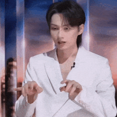 a man in a white suit is making a gesture with his hands .