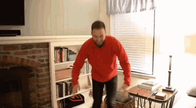 a man in a red sweatshirt is standing in front of a bookshelf