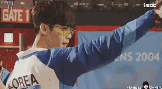 a man wearing sunglasses and a korea shirt is standing in front of a gate 1 sign .