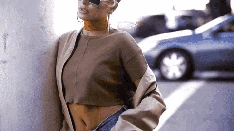 a woman wearing sunglasses and a choker is leaning against a wall .