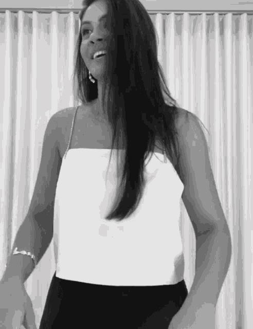 a woman wearing a white top and black skirt is dancing in front of a white curtain