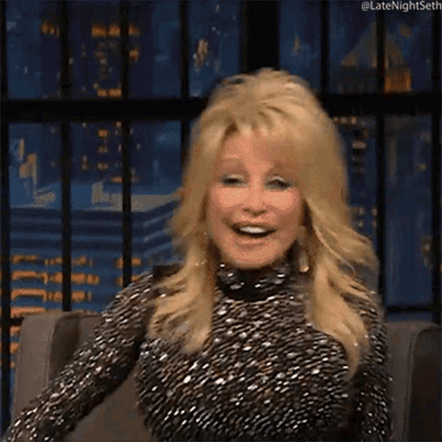 dolly parton is smiling while sitting in a chair in front of a city skyline .