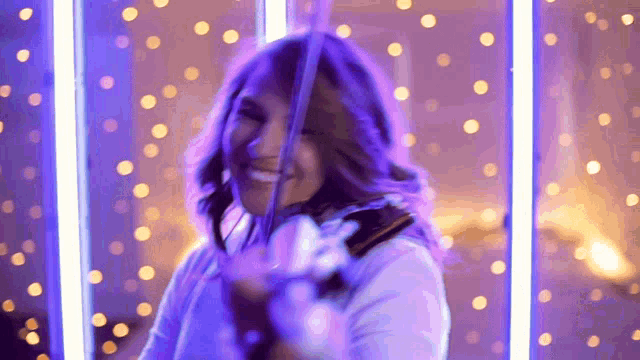 a woman playing a violin with purple lights in the background