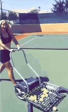 a woman is pushing a cart of tennis balls on a tennis court