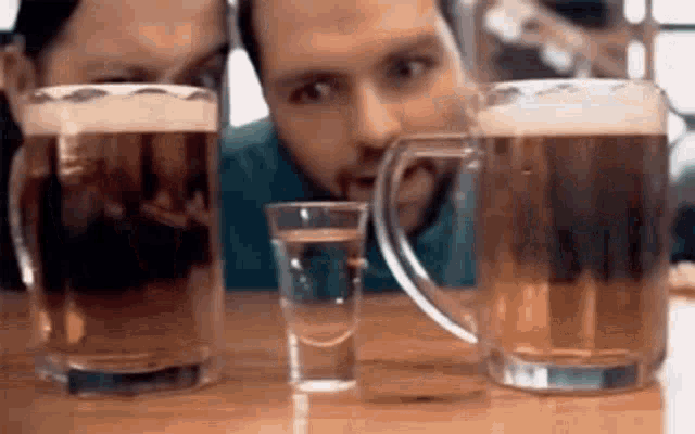 two men are sitting at a table drinking beer and shot glasses