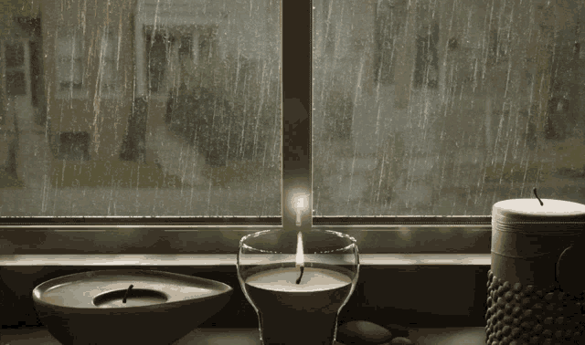 a candle is lit in front of a window with rain coming down outside