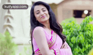 the woman is wearing a pink saree and smiling .