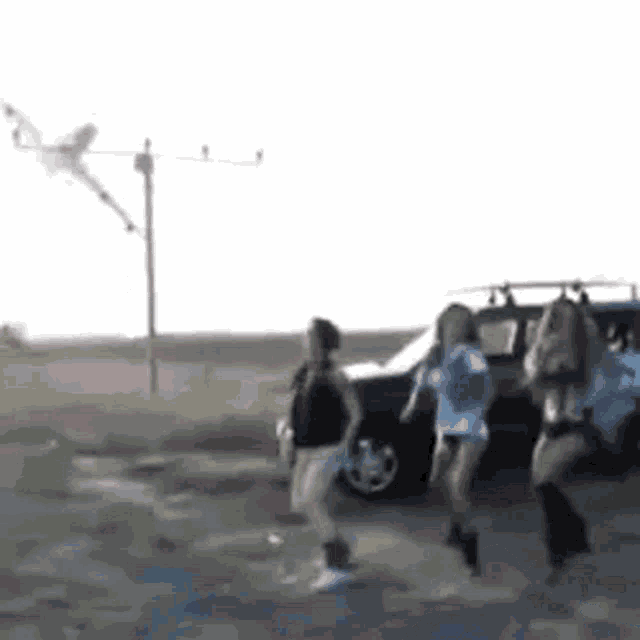 a group of women are dancing in front of a car while a kite is flying in the background .